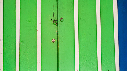 Puerta de madera verde con listones verticales blancos y detalles rústicos en un diseño simétrico