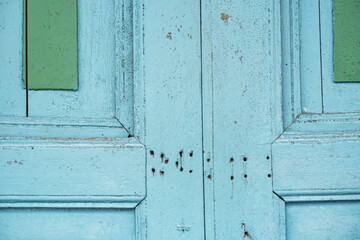 Primer plano de una puerta antigua de madera azul con detalles verdes y marcas de desgaste y agujeros visibles.