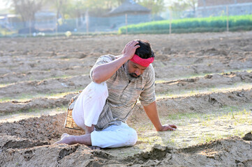Indian sad and discouraged farmer man sitting in the soil and lost deeply his dry agriculture field 