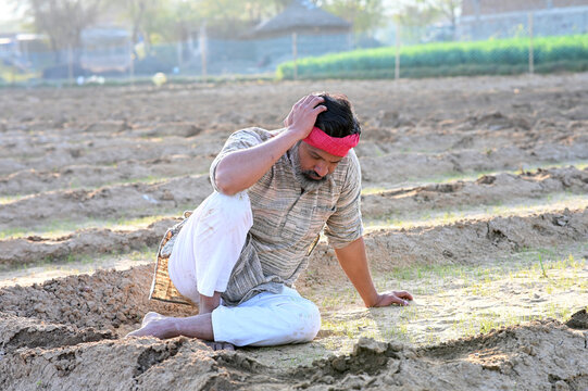 Indian sad and discouraged farmer man sitting in the soil and lost deeply his dry agriculture field 