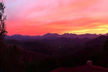Vibrant sunset paints the sky with fiery hues, casting a warm glow over rolling mountain silhouettes.  A peaceful scene perfect for relaxation or travel themes.