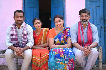 Indian happy rural family sitting on traditional bed in village. Rural complete family looking at the camera. Concept of rural family lifestyle. Group of rural people with senior man at village home.