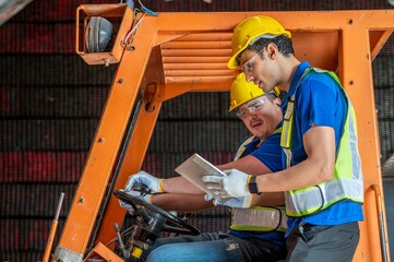 Two men in hard hats and safety vests operate a forklift in a warehouse. © BESTIMAGE