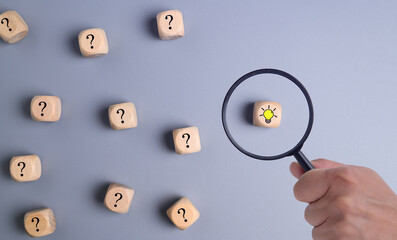 Hand holding magnifying glass focuses on light bulb with question mark around it, Symbol of...