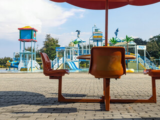 Picnic table with umbrella or patio set by the pool of a water park with blurred water rides in the...