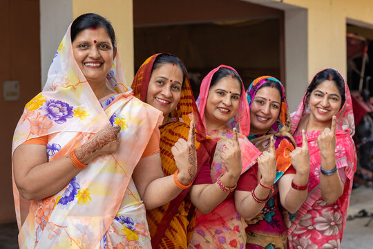Group of happy rural indian women standing in queue showing their finger marked with black ink after casting vote. Election in india.
