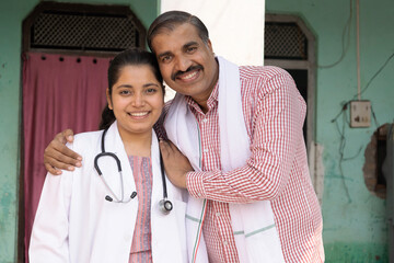 Happy Indian rural father embracing and support his young daughter wearing apron and stethoscope...
