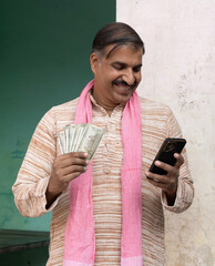 Happy Rural Man talking on phone while holding 500 Rupees Notes at village. The middle-aged Indian...