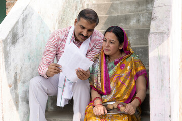 Portrait of an Indian rural couple looking household papers in village. Home loan, Finical...