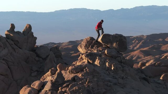 Slow motion drone shot of alone hiker man climbing on mountain peak