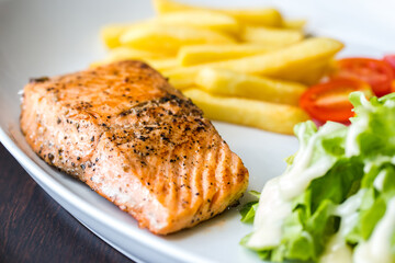 Grilled salmon steak with french fries tomatoes and vegetables