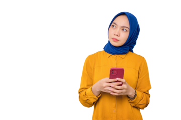 Pensive young Asian Muslim woman dressed in orange shirt holding mobile phone and looking aside at copy space, thinking about interesting offer isolated on transparent background
