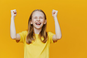 Happy girl celebrating success against a bright yellow background, showcasing joy and excitement in...
