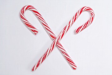 Red and white peppermint candy canes crossed on white background
