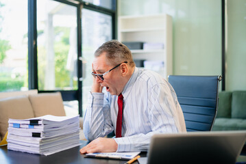 Obraz premium Senior businessman rips paperwork in rage at office desk. Workplace stress, anger, chaos, and burnout concept with files