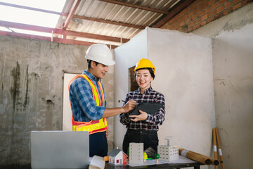 Engineers and contractors inspect construction plans indoors, using technology and equipment to...