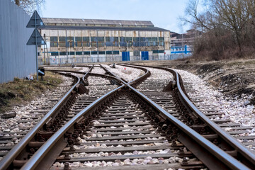 Rozjazd kolejowy przed budynkiem przemysłowym - halą fabryczną. Tory kolejowe rozgałęziają się w pobliżu budynku przemysłowego z dużą halą fabryczną. Tory są otoczone żwirem i biegną wzdłuż ogrodzenia © Grzegorz