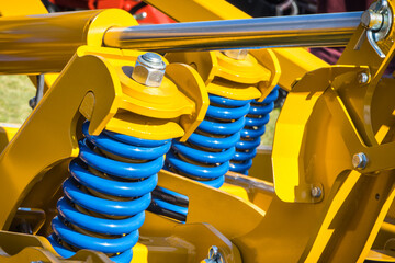 Steel blue spring as part of yellow heavy agricultural, industrial machine. Technology