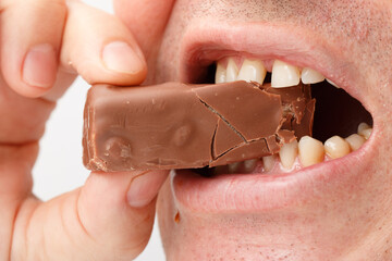 A man is eating a chocolate bar with his teeth showing