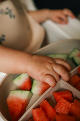 Close-up of toddler’s hands picking watermelon slices from a silicone plate on a highchair tray during a self-feeding mealtime
