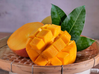 A ripe, juicy mango artfully presented on a woven bamboo tray. The mango is cut open, one half scored into neat, cube-like sections, slightly pushed outward to showcase the vibrant orange flesh.