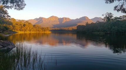 Serene lake reflecting the golden light on the mountains and surrounding trees at dawn, creating a peaceful and scenic vista, ideal for nature lovers and landscape photography enthusiasts