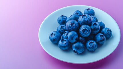 Plate of blueberries on a white plate. The blueberries are fresh and ripe. The plate is on a pink background