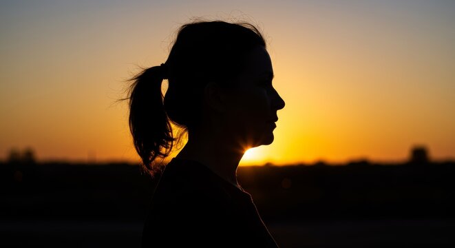 Silhouetted portrait of thoughtful woman against vibrant sunset backdrop