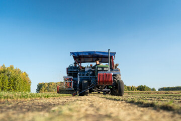 Obraz premium A Farm Tractor is Actively Working in the Open Field Beneath a Clear Blue Sky Above