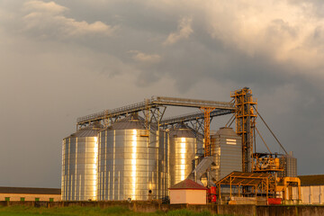 Group of grain dryers complex on dramatic cloudy sunset sky.