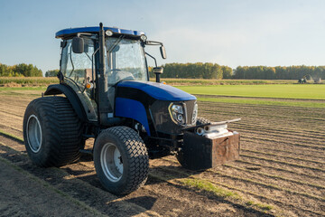 A Blue Tractor is Actively Working on a Lush Green Field at the Beautiful Sunrise Hour