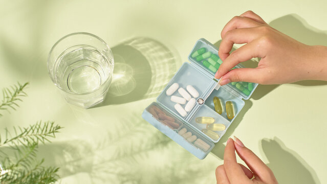 The patient is packing the pills into a personal pillbox to prepare for the trip. The pillbox contains different pills and placed in separate compartments for long-term storage. Medical concept.