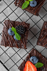 Chocolate brownies squares with chocolate glaze and fresh berries on top on a baking rack on a gray...