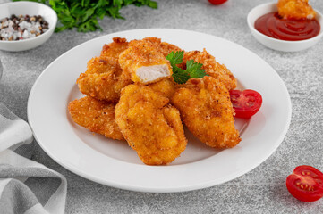 Crispy chicken nuggets with ketchup on a white plate on a gray concrete background.