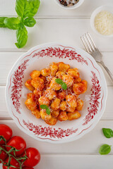 Traditional potato gnocchi with tomato sauce, parmesan cheese and fresh basil on a plate on a white wooden background. Italian cuisine. Top view, copy space.