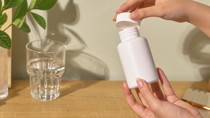 One hand is holding the bottom of the medicine bottle, the other hand is removing the cap from the...