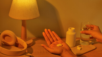 Top view of white pills placed in the palm. The pills are effective in treating headaches and helping patients sleep better. Compact table lamp, body made of natural wood, emits warm yellow light.