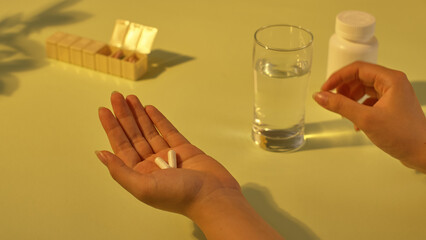 Two vitamin capsules are placed in the palm, with water next to it. The daily personal medicine box is placed far away. The medicine helps to provide nutrients and sleep well. Healthcare concept.