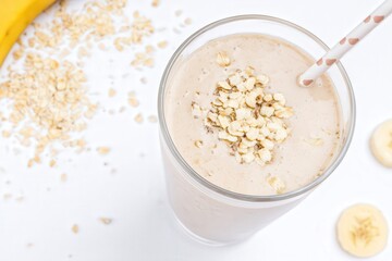 Glass of banana oat smoothie with fresh banana and oats on white background
