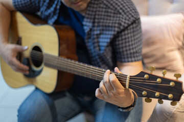 Fototapeta premium Detailed close-up of a man's hand pressing strings on a guitar neck. Intimate shot of musical practice and technique, taken indoors in a relaxed environment
