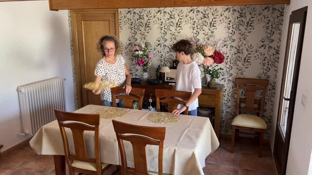 Mother and teenage son setting the dining table together in a cozy living room preparing for a family meal at home