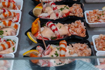 Sea street food for tourists on fish market on promenade in Oostende, Belgium, plastic box with variety of sea shells, shrimps, crab sticks, smoked fish