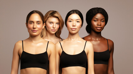 Confident group of four diverse young women with glowing skin standing side by side in black tops, representing beauty, skincare, and inclusivity across ethnicities against a soft neutral background.