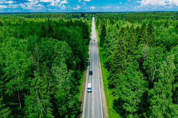 Aerial drone view of green summer woods and asphalt road with driving cars
