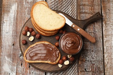 Chocolate hazelnut spread in bowl, nuts and toasts on wooden table, top view