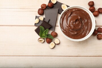 Chocolate hazelnut spread in bowl, nuts, pieces of chocolate and mint on wooden table, flat lay. Space for text