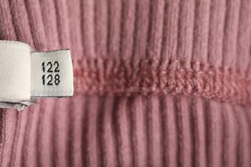 Clothing label with size on knitted garment as background, above view