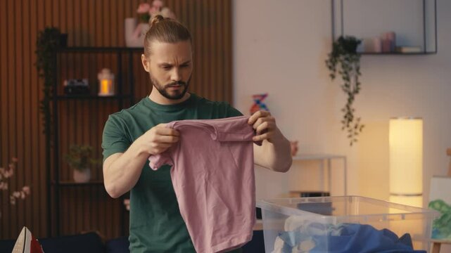 Frustrated man looking at shrunk t-shirt after laundry mistake, house chores