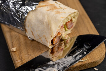 shawarma from thin wheat tortilla with meat with tomatoes and sauce, fast food made from various ingredients packed in foil