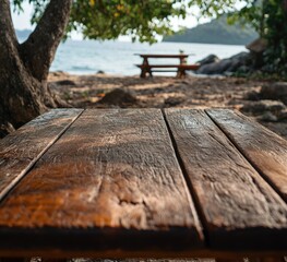 Fototapeta premium Close-up of a weathered wooden table on a sandy beach, with a blurry picnic table in the background